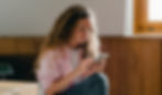 Woman with curly hair looking at her phone in an empty room with cardboard boxes